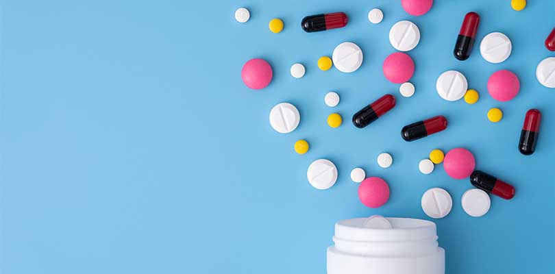 A white bottle with pills spilling out against a light blue background.