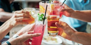 Four friends clinking glasses of colorful drinks together.