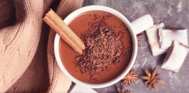 A mug of hot chocolate with chocolate shavings on top and a cinnamon stick.