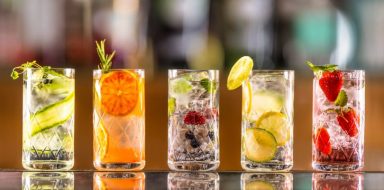 Five carbonated drinks lined up on a bar, with citrus fruits in them.